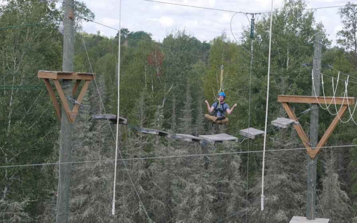 an outward bound student sits cross-legged while being suspended mid-air during a ropes course